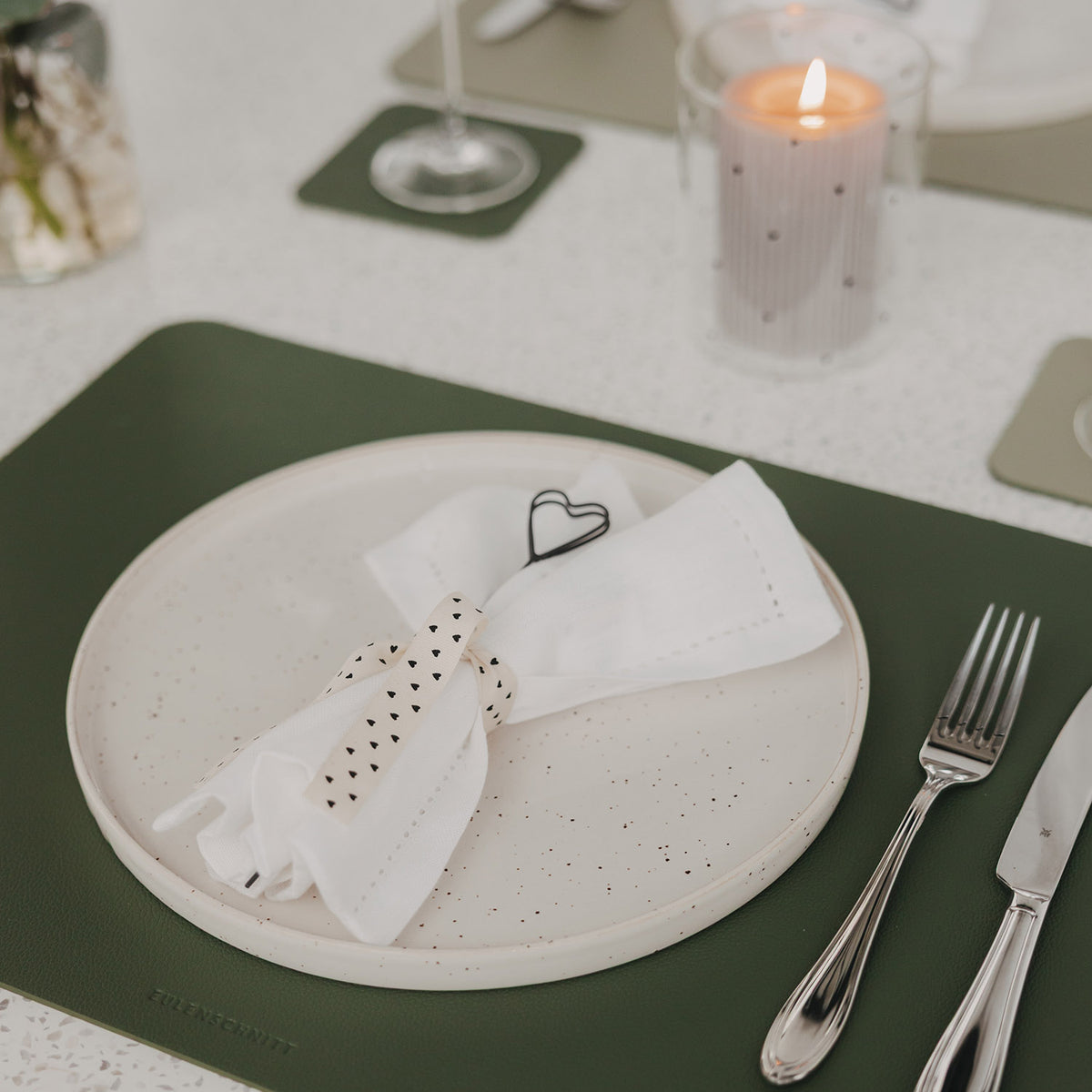 Dunkelgrünes Platzset mit Herzprägung, Teller, Serviette und Besteck auf gedecktem Tisch