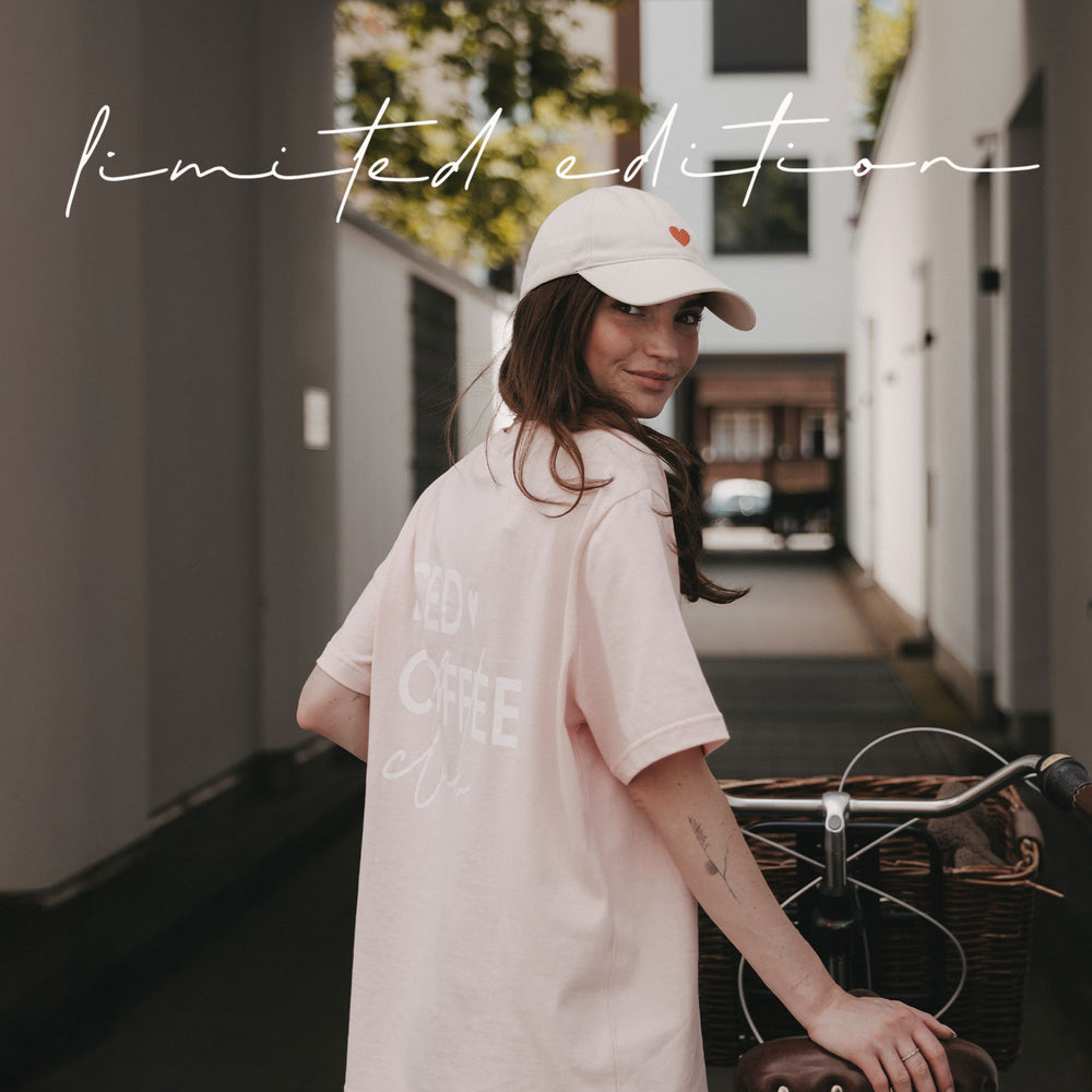 Frau mit beiger Cap und rosa Coffee T-Shirt neben einem Fahrrad