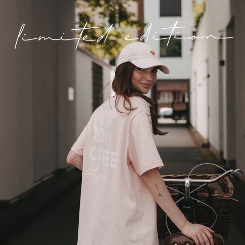 Frau mit beiger Cap und rosa Coffee T-Shirt neben einem Fahrrad