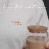 Detailaufnahme des weißen T-Shirts mit kleinem roten „Coffee Lover“-Print auf der Brust und Iced Coffee im Vordergrund.