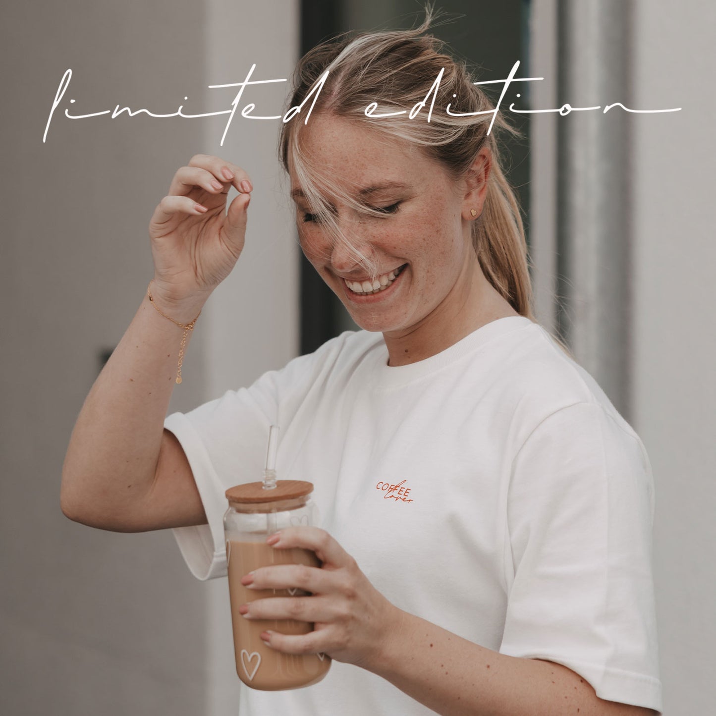 Lächelnde Frau im weißen „Coffee Lover“-T-Shirt hält einen Iced Coffee im Glas.