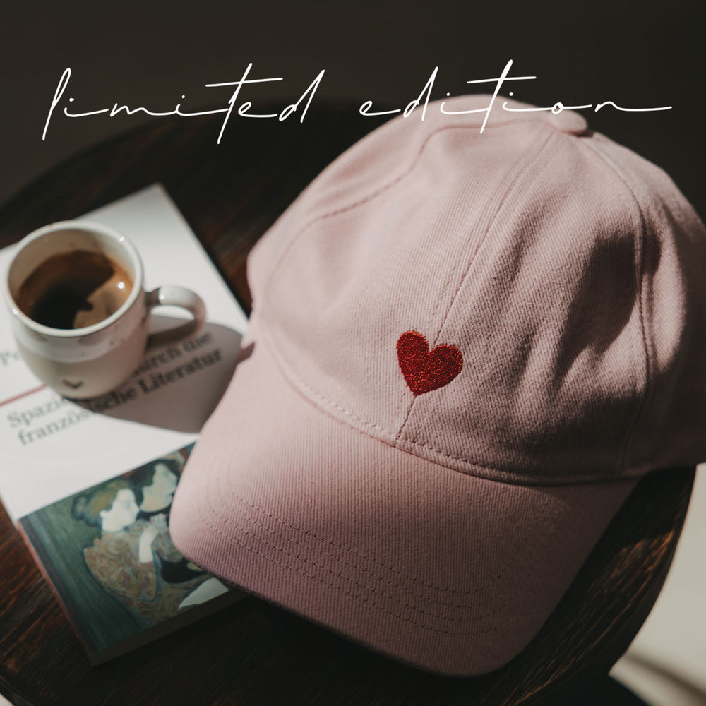 Rosa Cap mit roter Herz-Stickerei auf einem Tisch neben Kaffee und Magazin