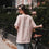 Rückansicht einer Frau im rosafarbenen Oversize-T-Shirt mit weißem „Iced Coffee Club“-Print neben einem Fahrrad.