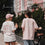 Zwei Frauen in weißem „Coffee Lover“- und rosafarbenem „Iced Coffee Club“-T-Shirt stehen mit Iced Coffee und Fahrrad auf der Straße.