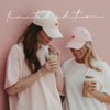 Zwei Frauen mit rosa und weißer Cap und Iced Coffee vor einer rosa Wand