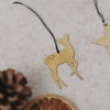 Detailaufnahme des goldenen Reh-Anhängers mit schwarzem Band, daneben Trockenscheiben und Zapfen.
