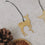Detailaufnahme des goldenen Reh-Anhängers mit schwarzem Band, daneben Trockenscheiben und Zapfen.