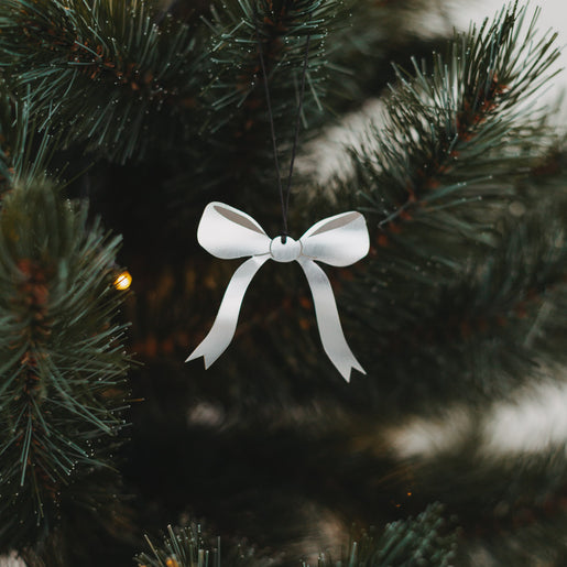 Silberner Schleifenanhänger aus Metall am Weihnachtsbaum mit Lichterkette, stilvoll und festlich dekoriert.