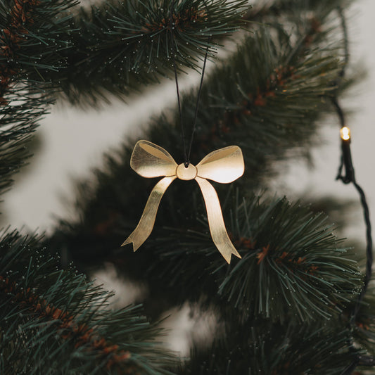 Goldene Metallschleife am Weihnachtsbaum, dekoriert mit schwarzem Band und Lichterkette.