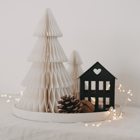 Schwarzes Metallhaus Mini mit Herz im Dach, dekoriert mit weißem Papierbaum, Tannenzapfen und Lichterkette.