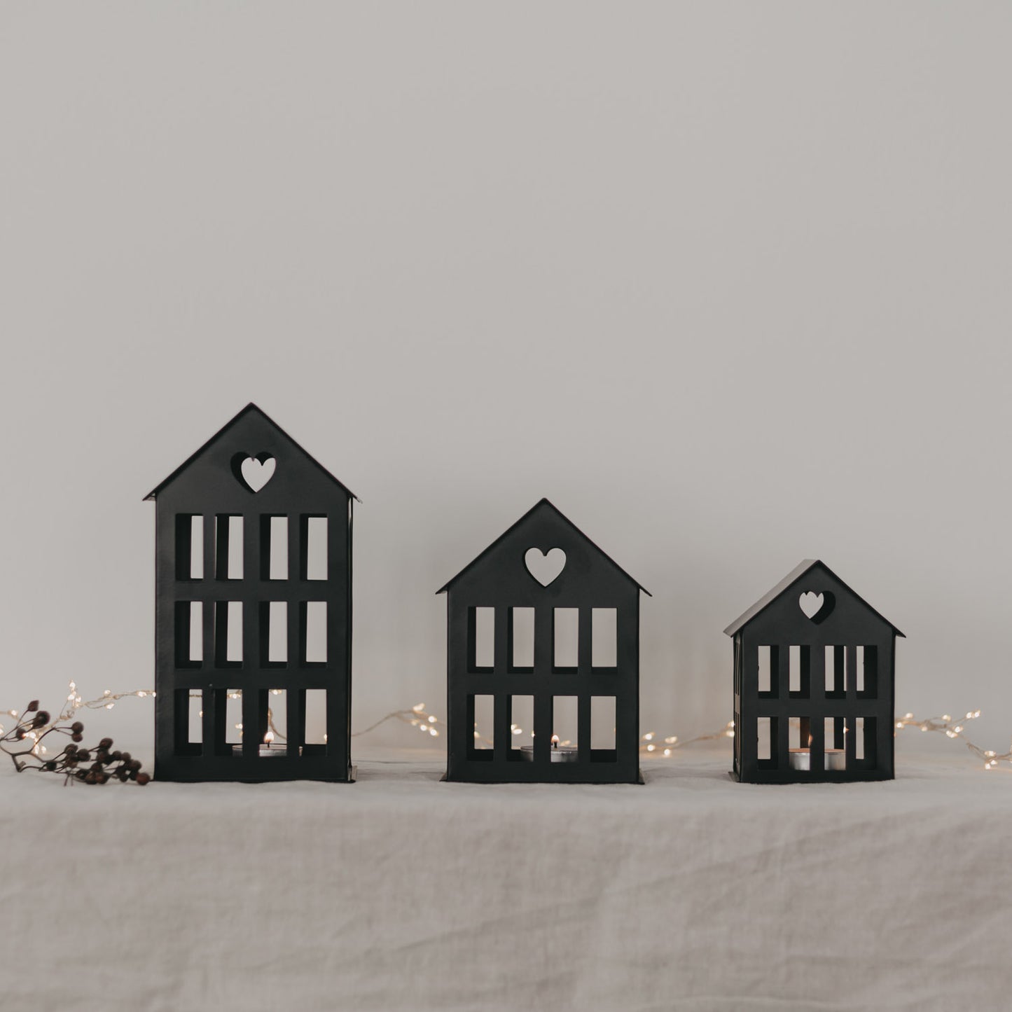 Drei schwarze Metallhäuser mit Herz im Dach und Lichterkette im Hintergrund – elegante Wohnraumdeko.