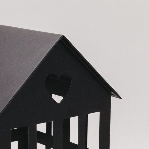Detailaufnahme des schwarzen Metallhauses mit Herzmotiv im Dach – moderne, minimalistische Dekoration.