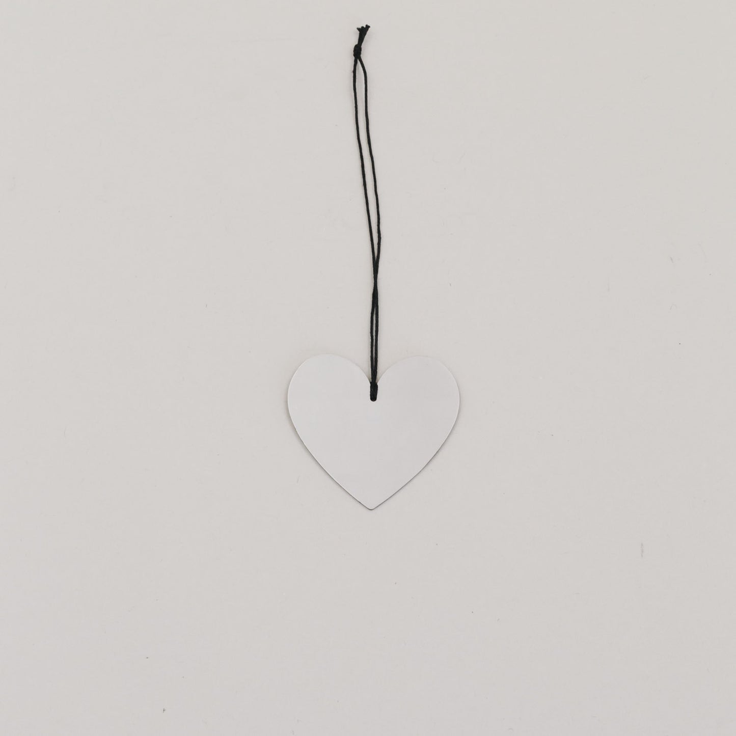 Metallanhänger in Herzform, silbern glänzend, mit schwarzer Kordel auf hellem Hintergrund