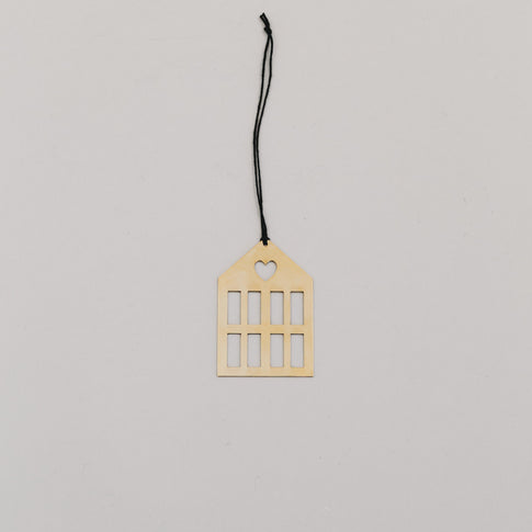 Goldener Hausanhänger aus Metall mit schwarzer Kordel auf hellem Hintergrund, minimalistisch arrangiert.