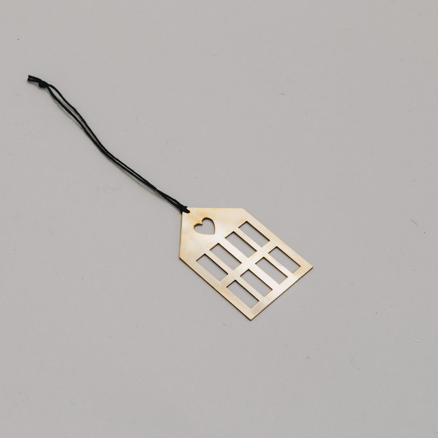 Schlichter goldener Hausanhänger aus Metall mit schwarzem Band, auf hellem Untergrund liegend.