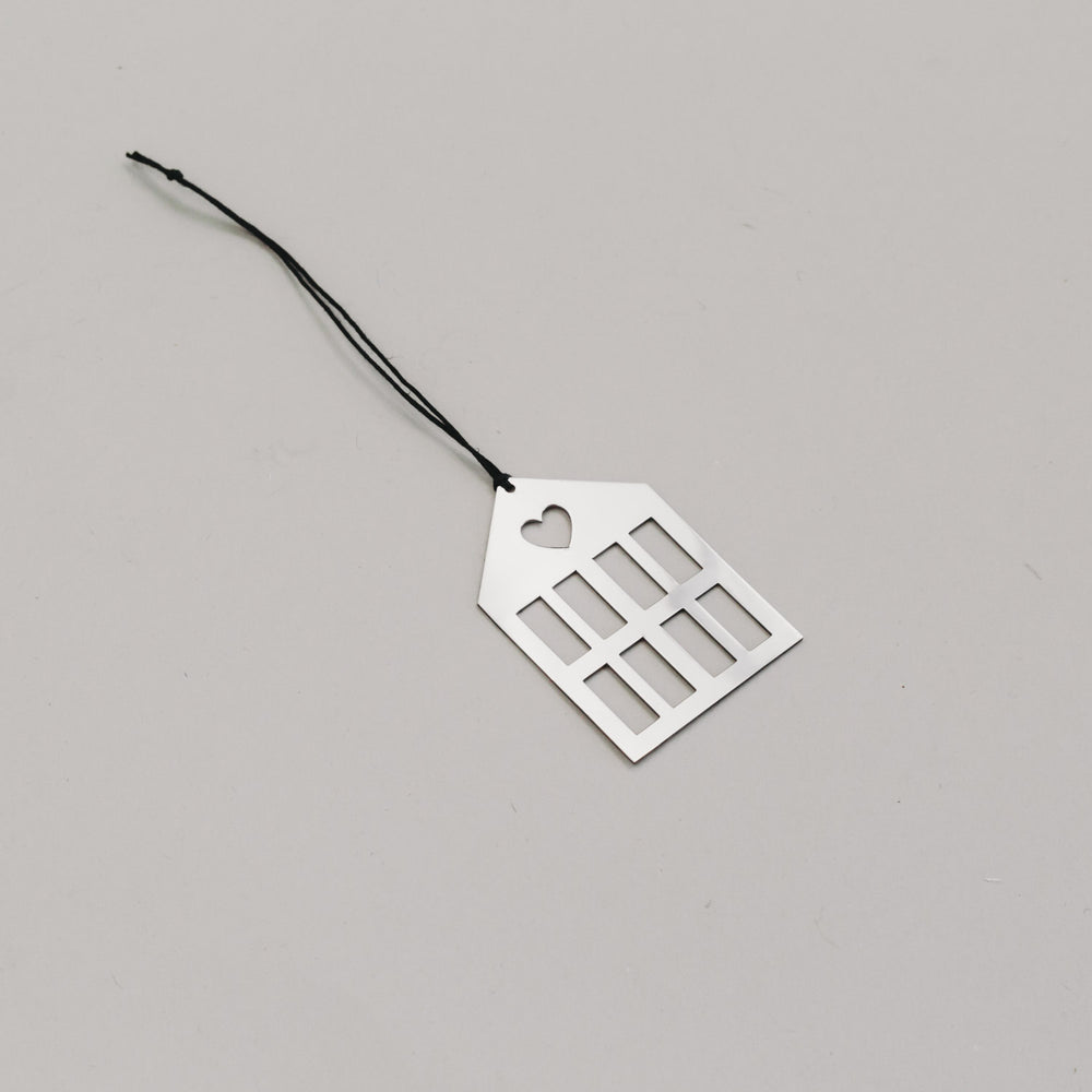 Schlichtersilberner Hausanhänger aus Metall mit schwarzem Band, auf hellem Untergrund liegend.