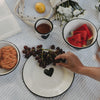 Weißer Emaille-Speiseteller mit schwarzem Herz im sommerlichen Picknick-Setting mit Weintrauben, Wassermelone und Emaille-Geschirr.
