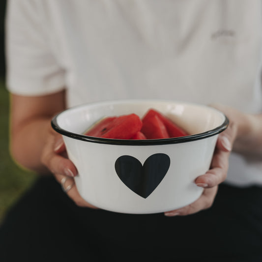 Weiße Emaille-Schale mit schwarzem Herz, gefüllt mit Wassermelonenstücken, wird mit beiden Händen gehalten.
