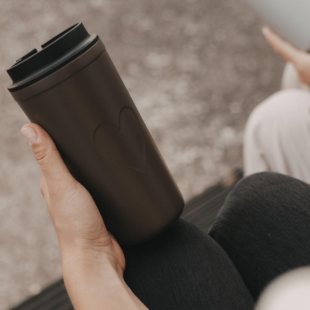 Brauner To-go-Thermobecher mit Herzmotiv und schwarzem Deckel in der Hand
