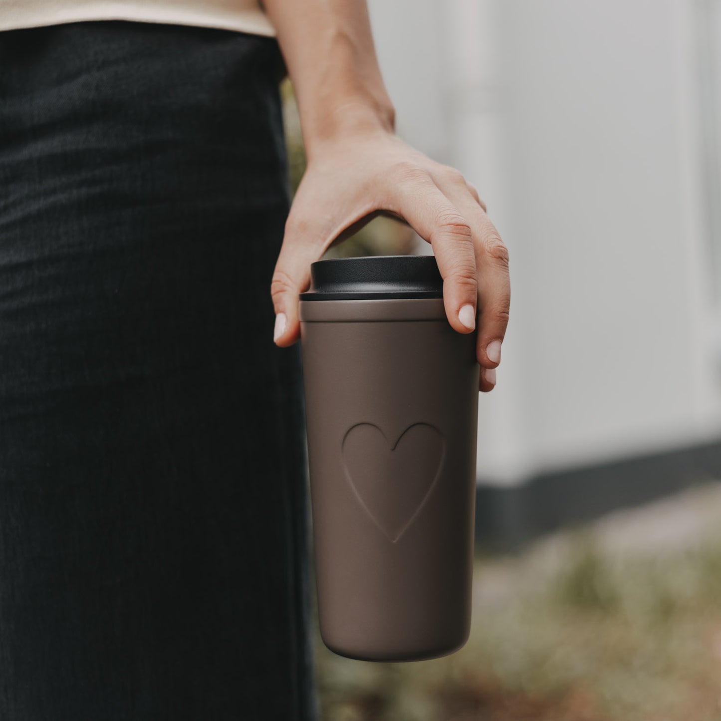 Brauner To-go-Thermobecher mit Herzmotiv und schwarzem Deckel beim Tragen