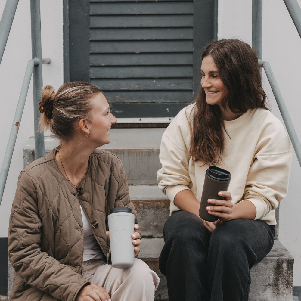 Zwei Frauen mit grauem und braunem To-go-Thermobecher mit Herzmotiv