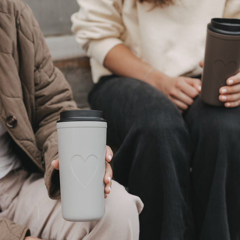 Grauer To-go-Thermobecher mit Herzmotiv und schwarzem Deckel in der Hand
