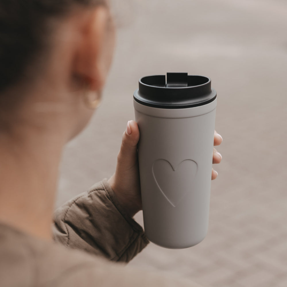 Grauer To-go-Thermobecher mit Herzmotiv und schwarzem Trinkdeckel in der Hand