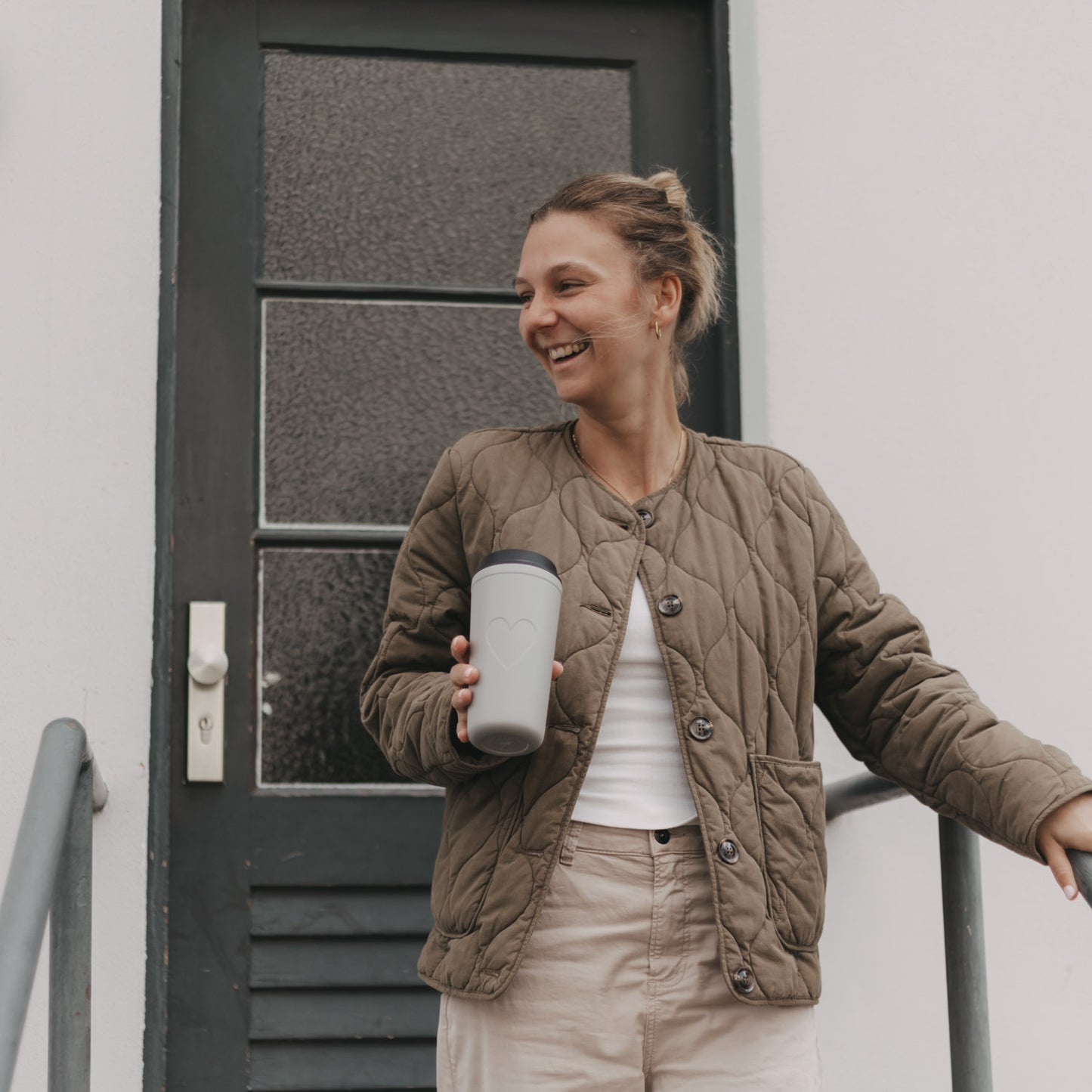 Frau mit grauem To-go-Thermobecher mit Herzmotiv und schwarzem Deckel