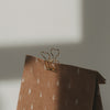 Goldener Foldback-Clip mit Herzmotiv an einer weihnachtlichen Geschenktüte aus Kraftpapier mit Tannenbäumen.