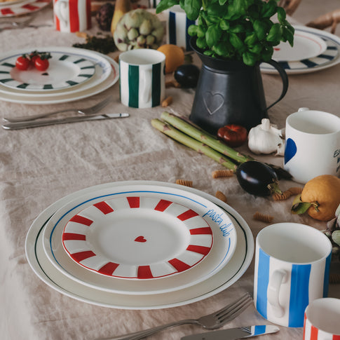 Gedeckter Tisch mit Porzellantellern, kombiniert mit Bechern und frischen Zutaten im natürlichen Setting.