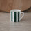 Kleine Tasse mit grünen Streifen frontal auf heller Fläche, dezenter Hintergrund mit Holzbrett.