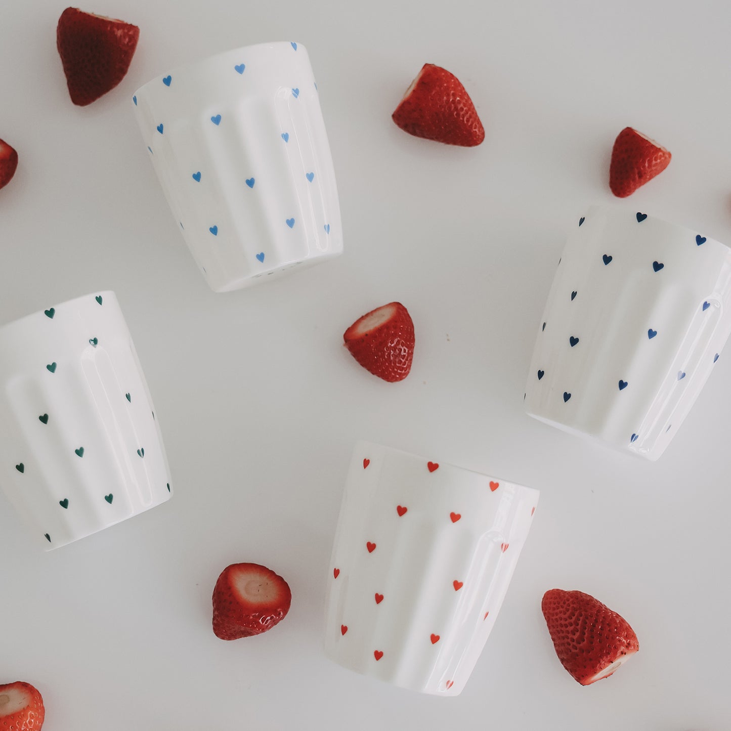 Vier Herzbecher mit Erdbeeren, farbige Herzmotive, dekorative Keramik Tassen im Flatlay