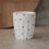 Weißer Becher mit kleinen roten Herzen auf Tisch, minimalistisch, Keramik Tasse für Kaffee oder Tee
