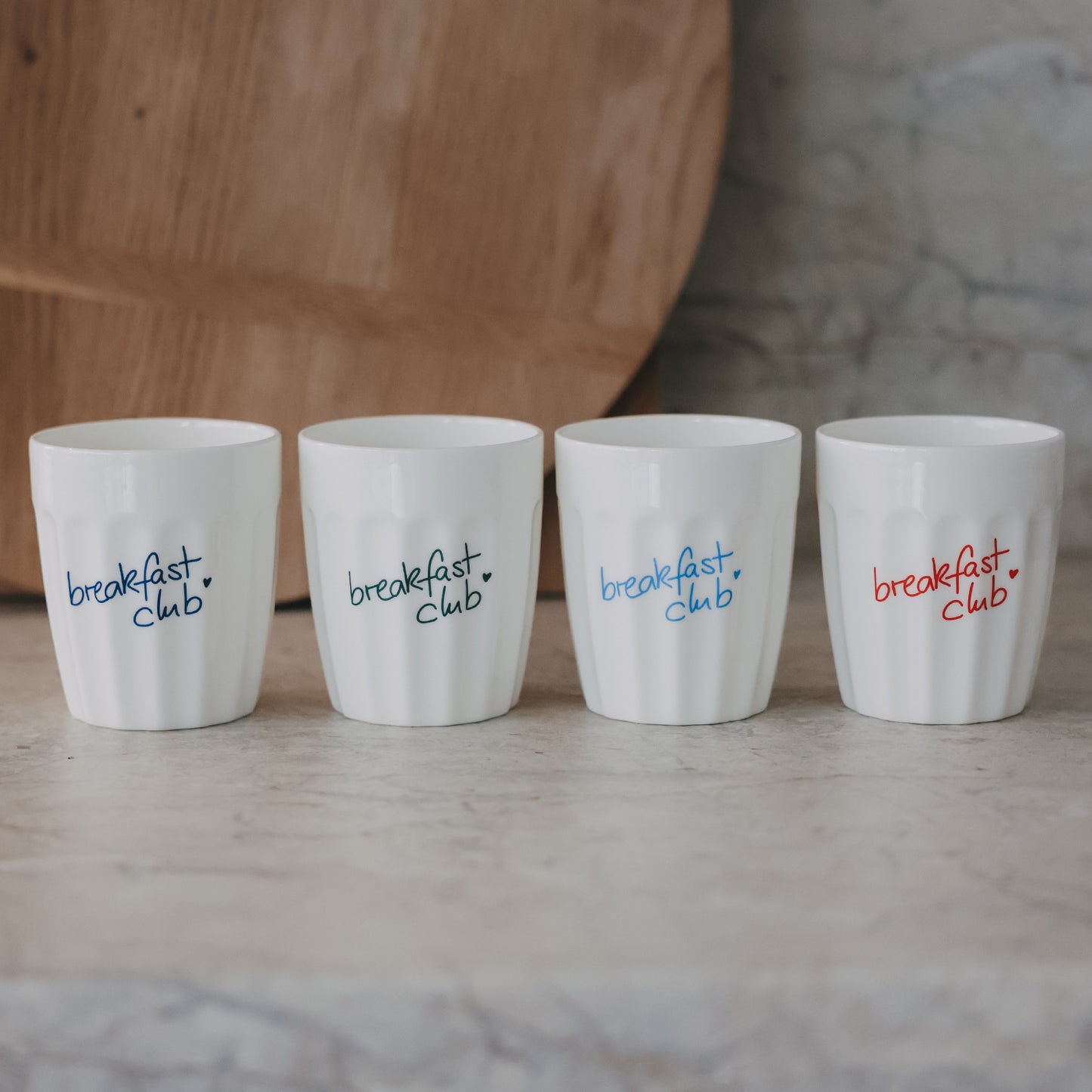 Vier weiße Keramikbecher „breakfast club“ mit bunten Schriftzügen auf neutralem Hintergrund