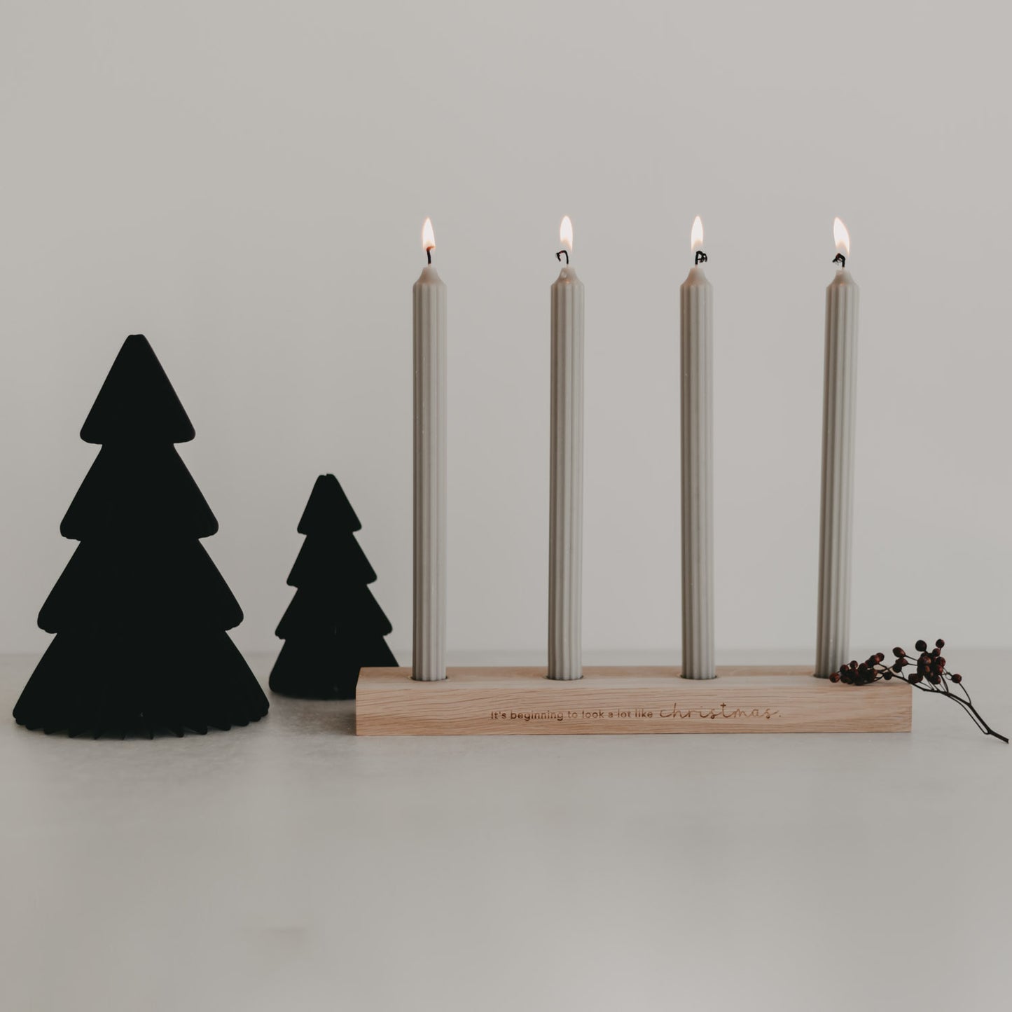 Schwarze Papiertannen mit Holz-Kerzenhalter und vier brennenden Kerzen – stilvolle, moderne Weihnachtsdeko auf Tischfläche.