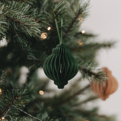 Grüner Papieranhänger aus Wabenpapier hängt dekorativ am geschmückten Weihnachtsbaum.
