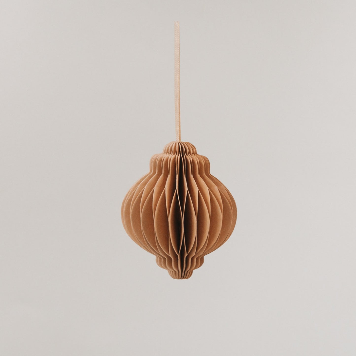 Brauner Papieranhänger mit Wabenstruktur, formschön und aufgehängt vor hellem Hintergrund.