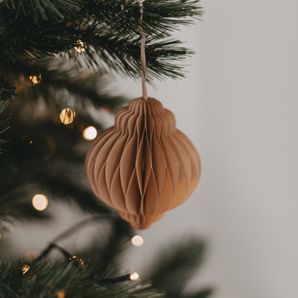 Brauner Papieranhänger dekorativ am Tannenbaum aufgehängt, mit sanfter Weihnachtsbeleuchtung im Hintergrund.