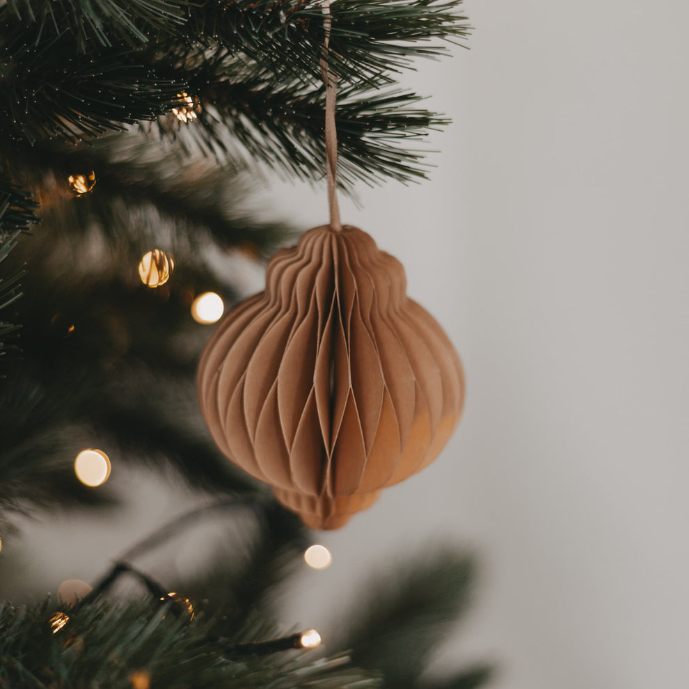 Brauner Papieranhänger dekorativ am Tannenbaum aufgehängt, mit sanfter Weihnachtsbeleuchtung im Hintergrund.