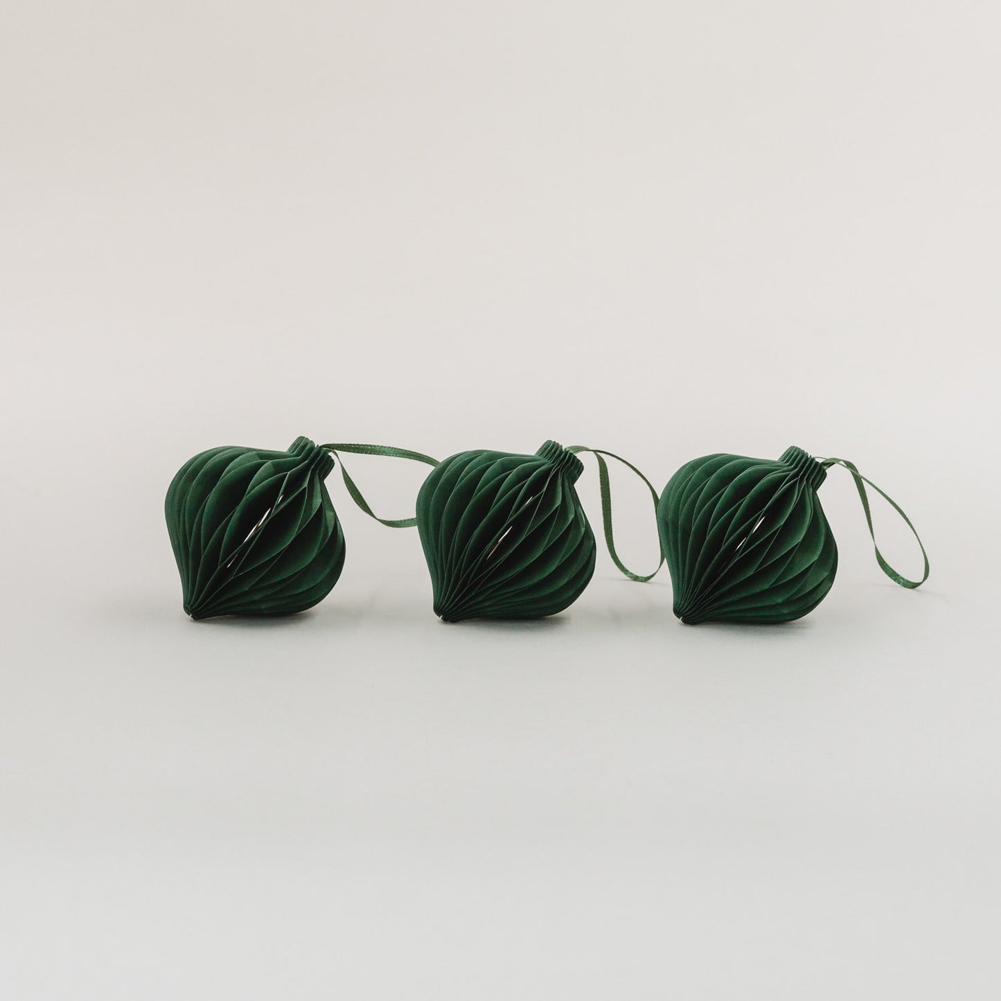 Drei dunkelgrüne Papieranhänger mit Wabenoptik aus dem 3er Set auf weißem Hintergrund nebeneinander liegend.