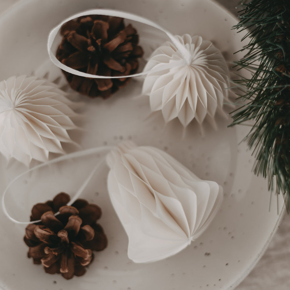 Papieranhänger Glocke natur kombiniert mit Zapfen und Ornamenten auf Dekoteller