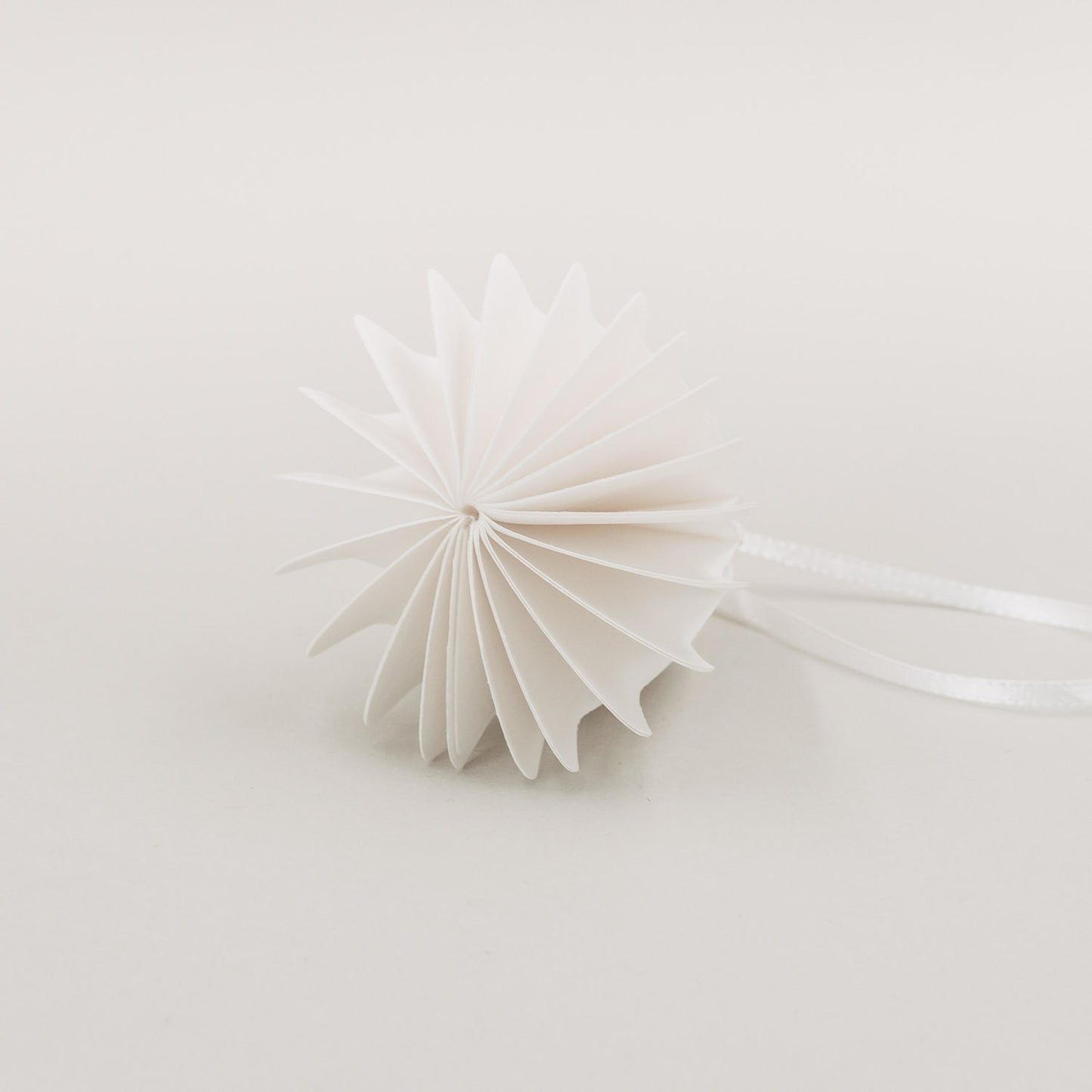 Weiße Papierglocke in Draufsicht zeigt elegante Wabenstruktur und feine Faltung mit Schleifenband.