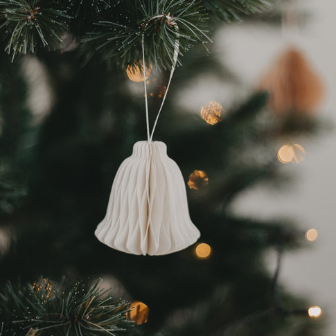 Weißer Papieranhänger in Glockenform mit Wabenstruktur am Tannenzweig mit Lichterkette