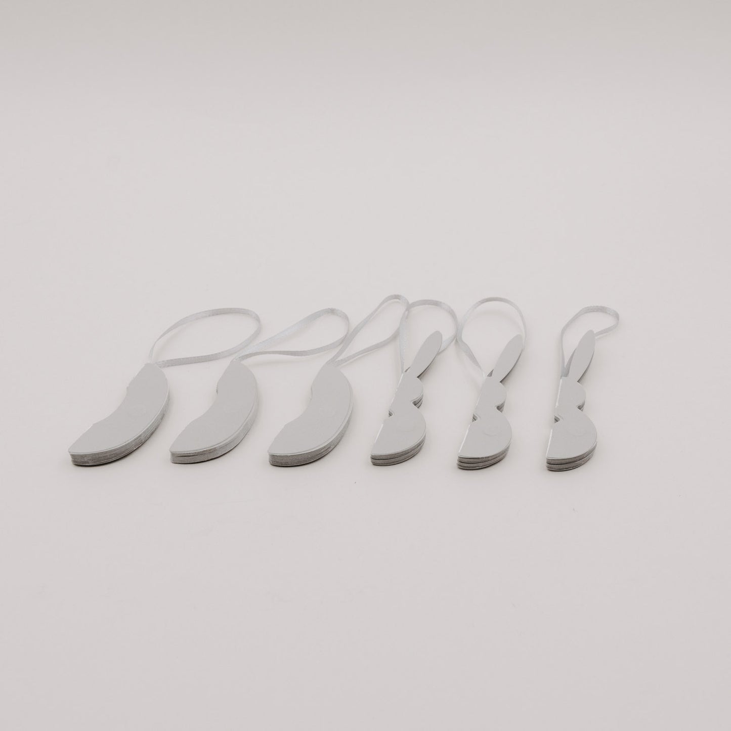 Sechsteiliges Set grauer Papieranhänger in Ei- und Hasenform, flach zusammengelegt.