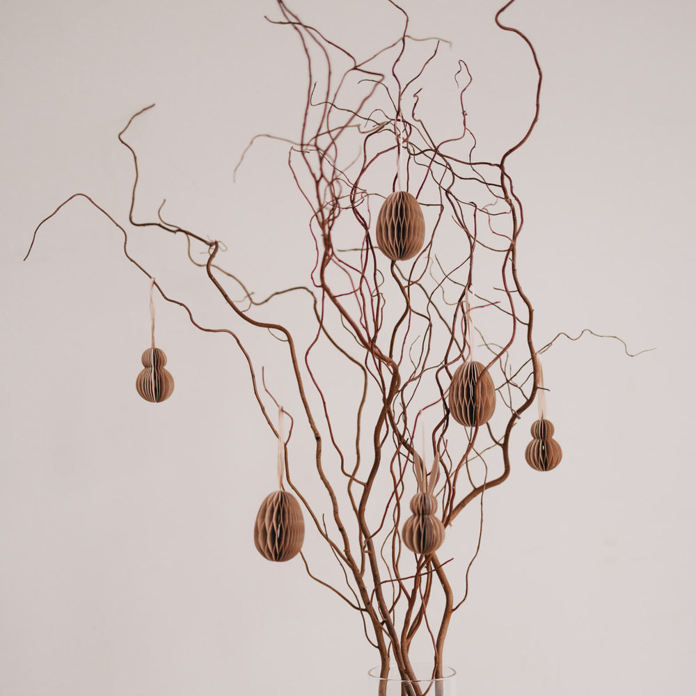 Natürliche Papieranhänger in Ei- und Hasenform hängen an dekorativen Zweigen in einer Vase.