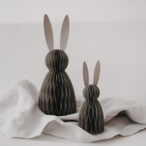 Zwei graue Papierhasen in kleiner und großer Größe als moderne Osterdeko auf hellem Stoff.