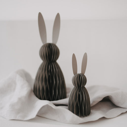 Zwei graue Papierhasen in kleiner und großer Größe als moderne Osterdeko auf hellem Stoff.
