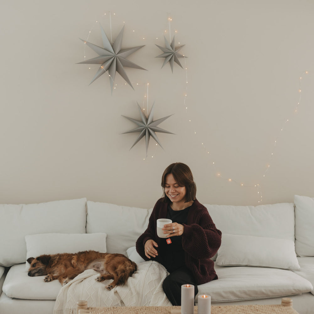 Graue Papiersterne mit Lichterkette als minimalistische Weihnachtsdeko über einem weißen Sofa