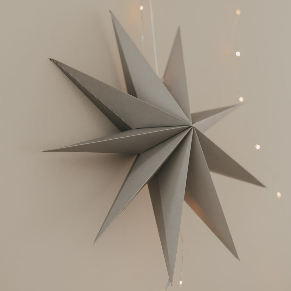 Grauer Papierstern mit filigranen Spitzen und warmer Lichterkette als moderne Weihnachtsdekoration