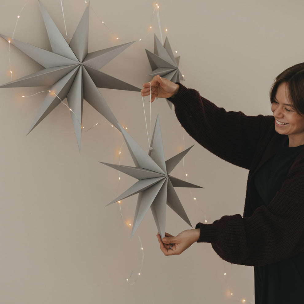 Graue Papiersterne in verschiedenen Größen mit Lichterkette als minimalistische Weihnachtsdekoration